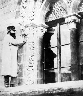 Black and white photo of a man carving the decorative archway of a window