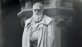 A stone statue of a bearded man, hands crossed at his front, shoulders draped in a cloak