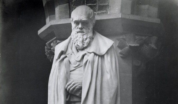 A stone statue of a bearded man, hands crossed at his front, shoulders draped in a cloak