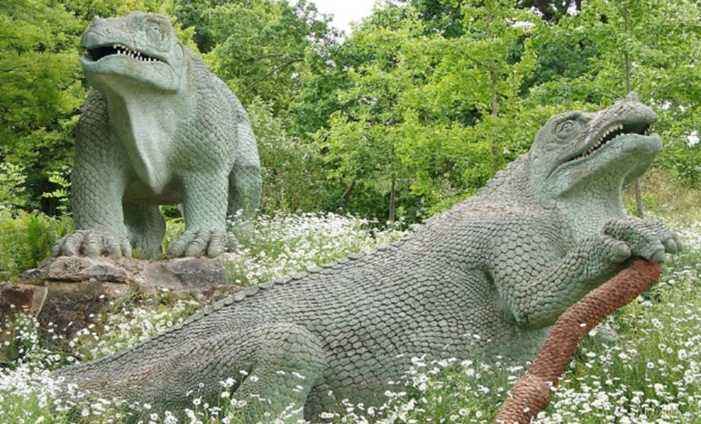 Two green dinosaur models surrounded by trees and meadow flowers