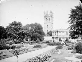Black and white photograph of borders, paths, and trees with spired tower in background
