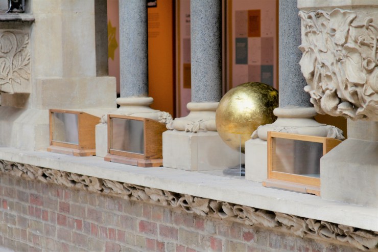 A golden sphere sitting on a stone balcony between stone columns and carvings