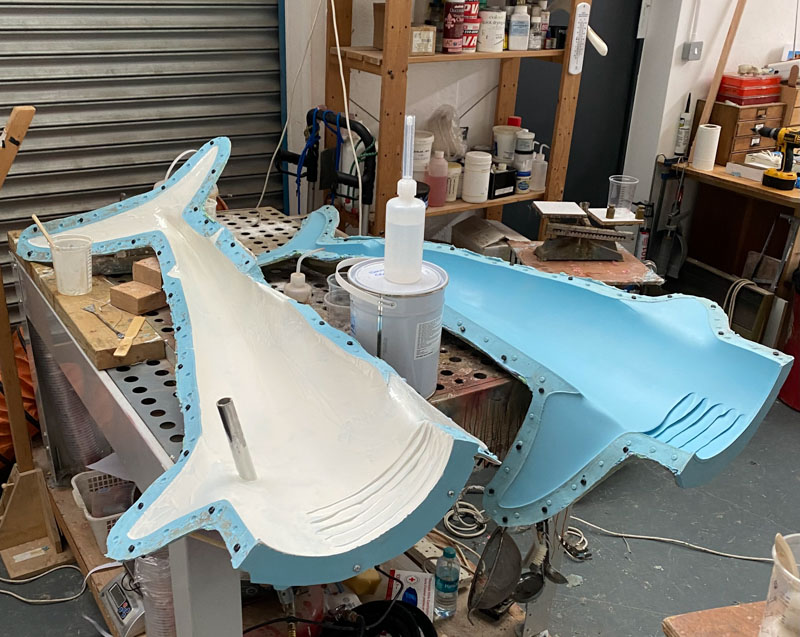 A workshop scene showing a silicone model of shark's body cut into two halves lengthways and laying on a workbench. The interior of the mould is light grey and the exterior is light blue.